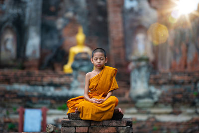 Boy wearing traditional clothing meditating while sitting outdoors