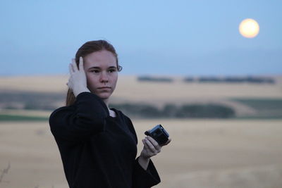 Woman looking away while holding camera at field