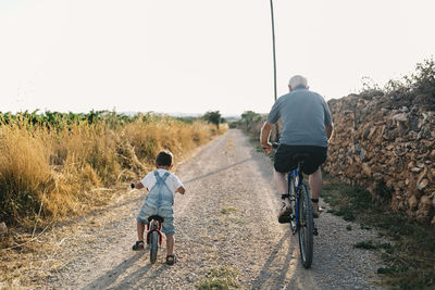 Back view of little boy and his great-grandfather on bicycle tour