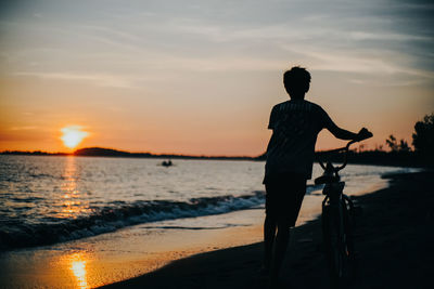 Rear view of silhouette man on beach against sky during sunset