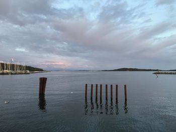 Wooden posts in sea against sky