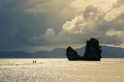 Silhouetted people seemingly walking on water leading to an island