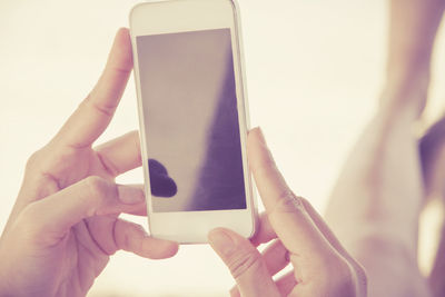 Close-up of man photographing through mobile phone against sky at beach