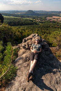 Full length portrait of woman sitting on landscape against mountains