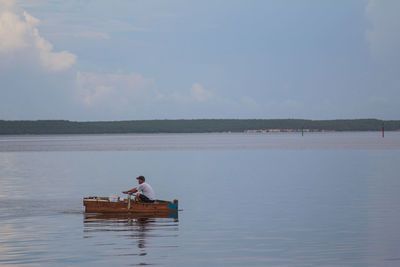 Man sitting on boat over lake against sky