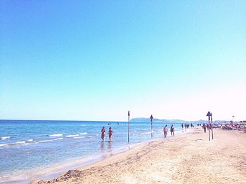 People on beach against clear blue sky