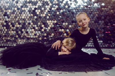 Two girls in black dresses sit on the floor in a sequined studio