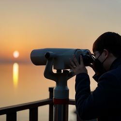 Side view of man looking sky through telescope during sunset