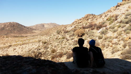 Rear view of people sitting on desert against clear sky