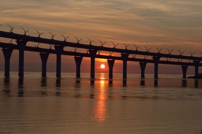 Silhouette bridge over sea against sky during sunset