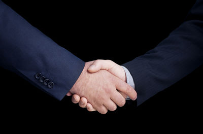 Cropped image of business people shaking hands against black background