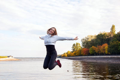 Full length of man jumping in lake against sky