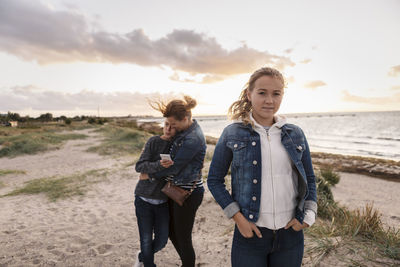 Portrait of teenager girl while mother embracing son at beach