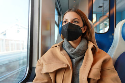 Young thoughtful woman wearing black medical face mask on train looking through the window
