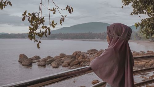 Rear view of woman by lake against sky