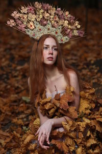 Thoughtful young woman wearing flowers on hair sitting at forest during autumn