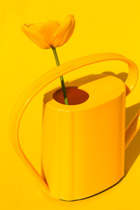 Close-up of red watering can against yellow background