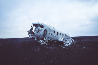 Abandoned airplane on field against cloudy sky