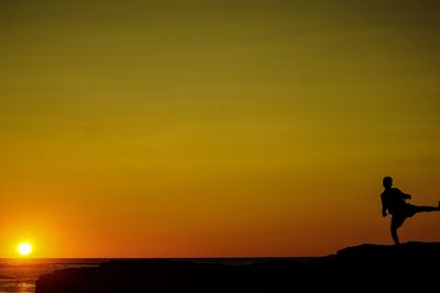 Silhouette man standing on rock against sky during sunset