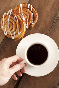 Cropped hand having black coffee and cookies on table