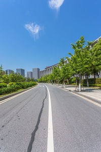 Road by trees in city against sky