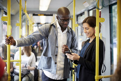 Multi-ethnic commuters sharing smart phone while standing in tram