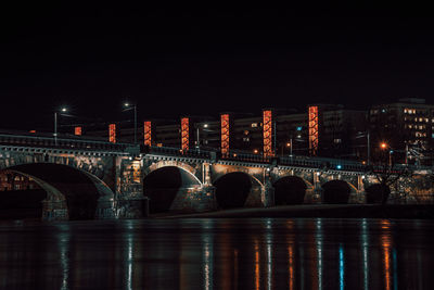 Arch bridge over river against sky in city at night