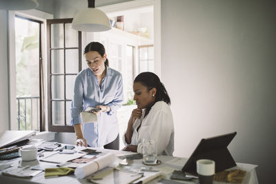 Female architects discussing about fabric swatch while working at table in home office