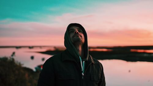 Man looking up while standing against lake during sunset