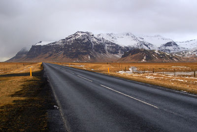 Empty road by snowcapped mountains against sky