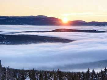 Pink orange sun rise above misty winter mountains, shinning fog. peaks above creamy mist in valley.