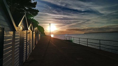 Footpath amidst sea against sky during sunset