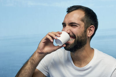 Man drinking coffee against glass with sea in background