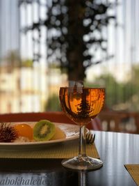 Close-up of fruits with wineglass on table against window