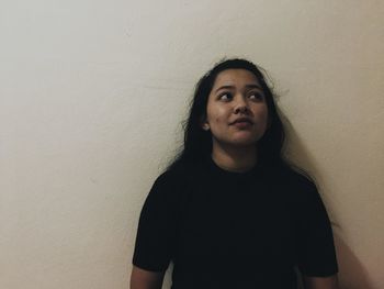 Young woman looking away while standing against wall