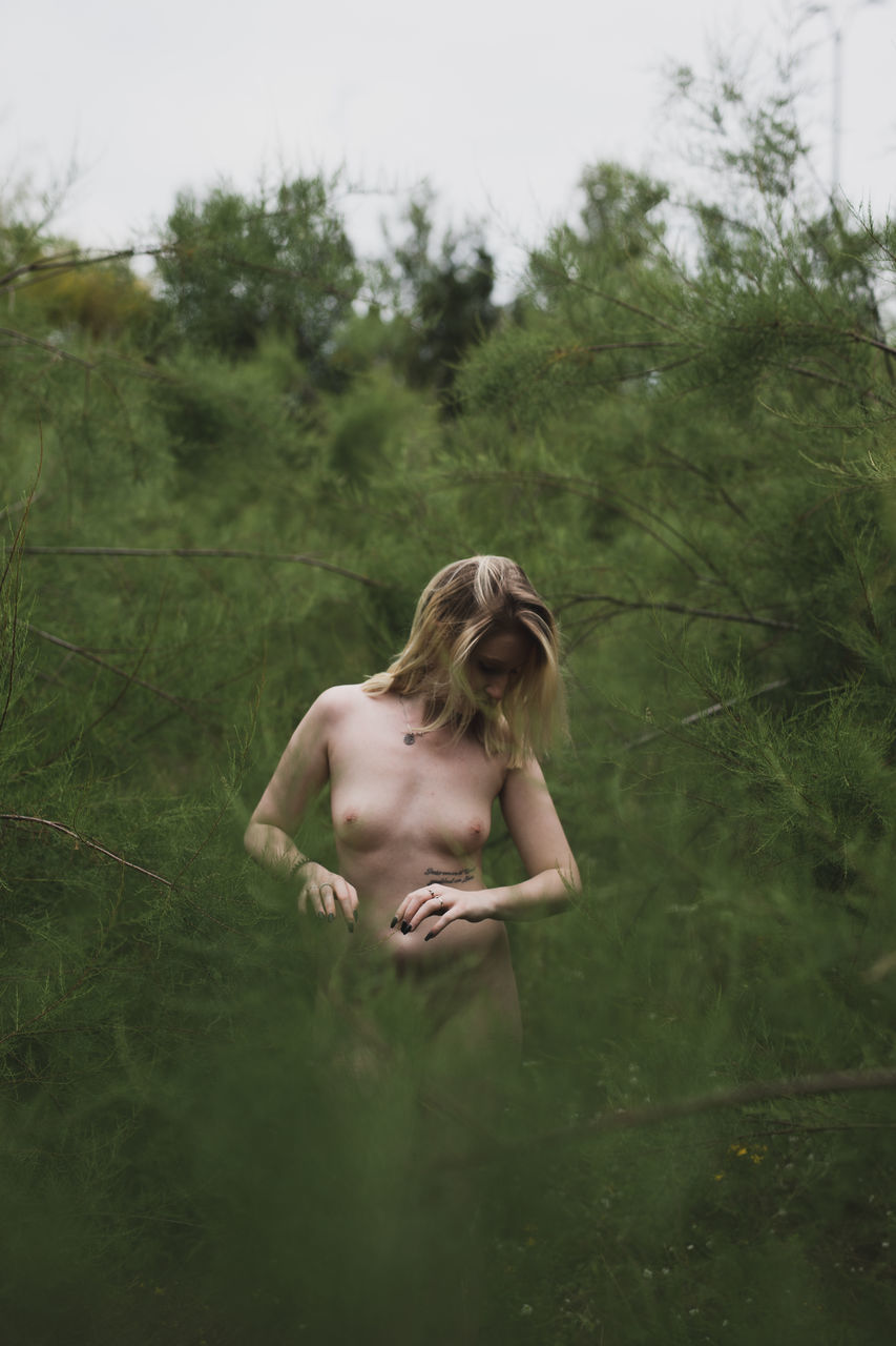 Young naked woman standing in forest