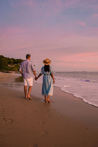 Rear view of couple holding hands walking on beach