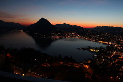 Illuminated city by mountains against sky at sunset