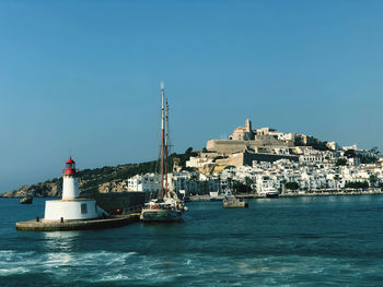 Sailboats in sea by buildings against clear sky