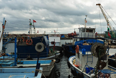 Boats at harbor against cloudy sky