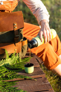 Midsection of woman pouring water in cup while sitting outdoors