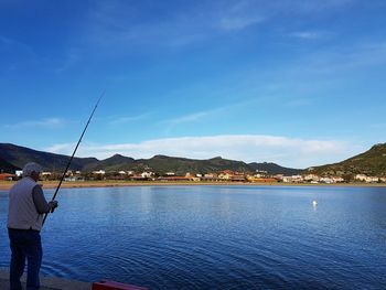 Rear view of senior man fishing on lakeshore against sky