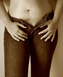 Midsection of woman with unbuttoned jeans standing at home