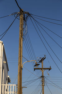 Low angle view of electricity pylon against clear blue sky