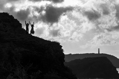 Silhouette people standing on rock against sky