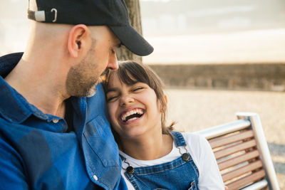 Father looking at daughter laughing while sitting on bench