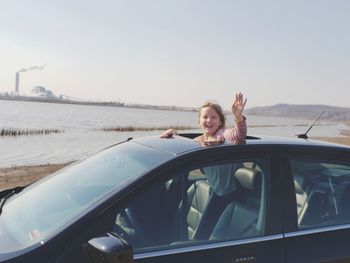 Portrait of smiling girl waving hand while looking through sun roof