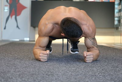 Full length of shirtless man doing push-ups on floor in gym