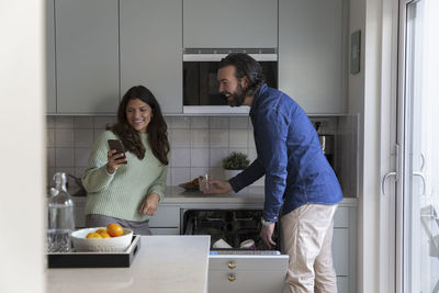 Smiling woman sharing smart phone with man in kitchen