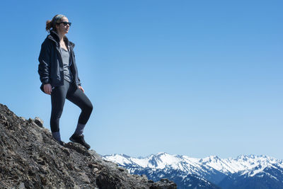 Low angle view of young woman standing on cliff against clear blue sky